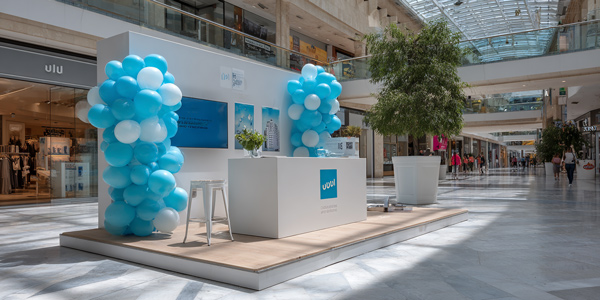 Stand de cartón decorado con globos y carteles en centro comercial, usado como elemento de PLV para captar atención