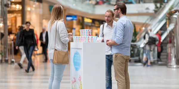 Personas recibiendo muestras gratuitas en un stand de centro comercial, ejemplo real de sampling en tienda para aumentar ventas