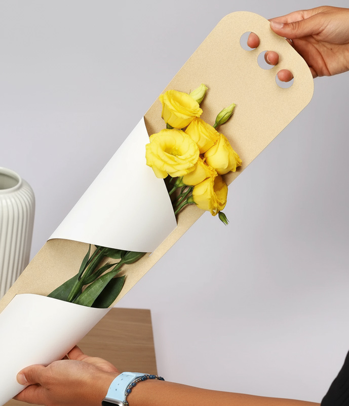 Persona sosteniendo ramo de flores amarillas en packaging de cartón y papel blanco para presentación floral