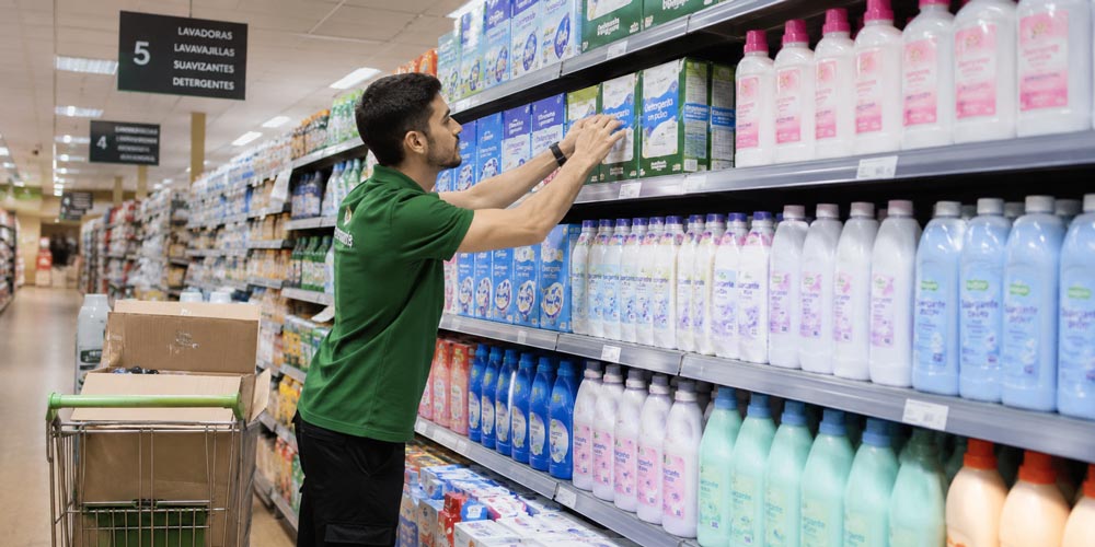Empleado reponiendo productos de detergencia en el lineal de un supermercado